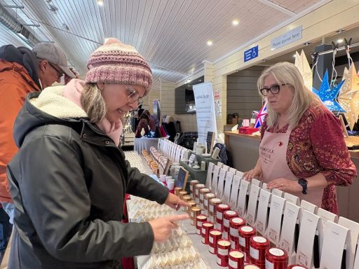 A woman browses products at a market stall while another woman assists her.